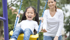 Image of a girl on a swing with her mom pushing from behind