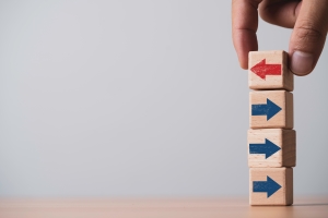 A hand adjusting stacked wooden blocks with arrows, reversing one direction to represent deviation from standard procedures.