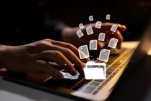 A person typing on a laptop with floating digital document icons, representing review of multiple files or data sources.